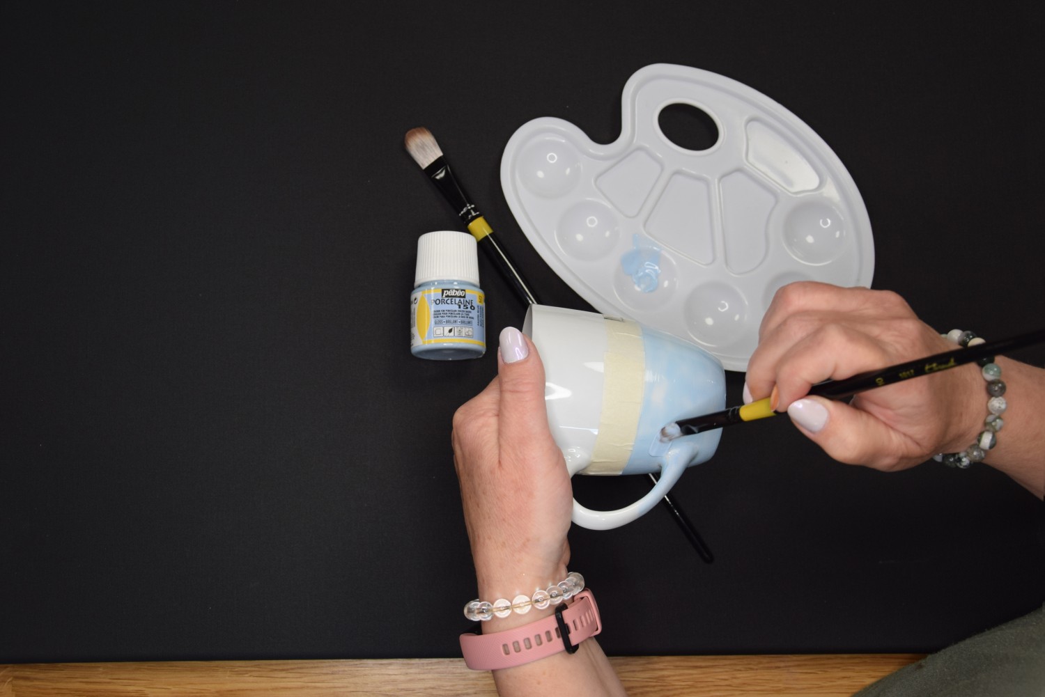 Žena používa bledomodrú farbu na porcelán a natiera s ňou spodnú stranu hrnčeka.